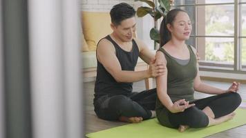 casal de família feliz asiático lindo estilo de vida, mulher fazendo ioga sentada, meditando na pose de lótus, treino em casa e o homem massagem no ombro para relaxar. conceito de esporte saudável