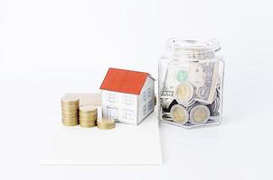 Ahorrando dinero con botellas de vidrio y casa de papel y pila de monedas. foto