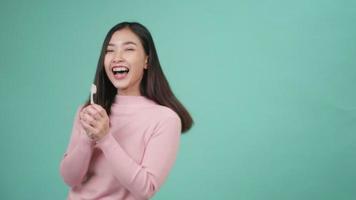 asiatico giovane bella donna sorriso lavarsi i denti ballare godendo la musica, femmina spazzolare i denti cantando canzone, ballare e divertirsi isolato su sfondo blu, stile di vita igiene dentale e concetto di salute video