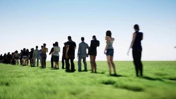 moviéndose al lado de una cola de personas en el fondo de un campo de hierba verde video