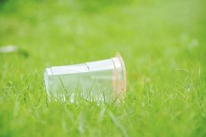 primer plano transparente taza de plástico recicla basura en el campo de hierba verde en el parque con la naturaleza de la frescura de la hierba. concepto de limpieza foto