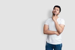 Asian handsome man on white t-shirt having doubts while looking up over isolated white background photo