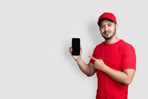 Delivery man employee in red cap blank t-shirt uniform hold black mobile phone application isolated on white background photo