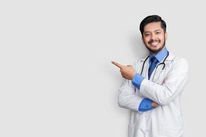 Doctor wearing uniform smiling while presenting and pointing isolated on blue background with copy space photo