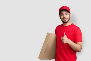 Delivery man employee in red cap blank t-shirt finger uniform hold empty cardboard box isolated on white background photo