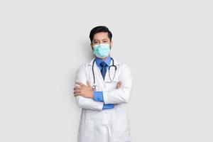 Young male doctor face covered with mask and arm cross over isolated background, health concept photo