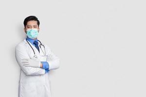 Young male doctor face covered with mask and arm cross over isolated background, health concept photo