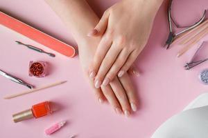 Nail care procedure in a beauty salon. Female hands and tools for manicure on pink background. Concept spa bodycare. photo