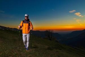 Young man with beard practicing nordic walking in a colorful sunset photo