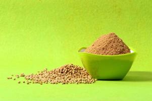 Coriander seeds and Powdered coriander in green container on green background photo