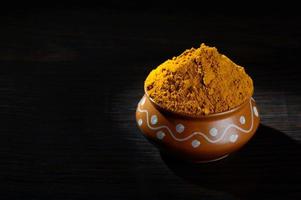 Turmeric powder in clay pot with roots or barks on black background photo