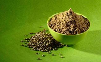 Coriander seeds and Powdered coriander in green container on green background photo