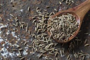 Cumin seeds in wooden spoon on a textured background photo