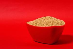 yellow mustard seeds in red bowl isolated on red background photo