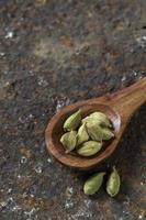 Cardamom pods in wooden spoon on a textured background photo