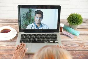 Consulta en línea con el médico en una computadora portátil y sosteniendo un contenedor de pastillas médicas foto