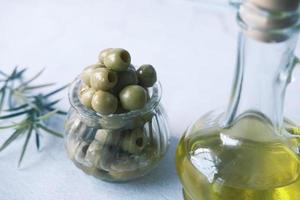 bottle of olive oil and fresh olive in a container on table . photo