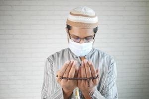 muslim man with face mask keep hand in praying gestures during ramadan, photo