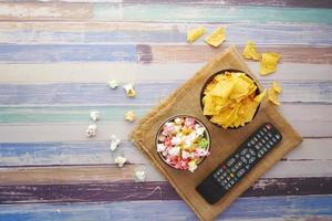 Vista de ángulo alto de palomitas de maíz, patatas fritas y control remoto de TV en la mesa foto