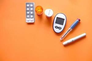 insulin pen, diabetic measurement tools and pills on orange background photo