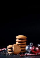 Galletas - Pila de deliciosas galletas de crema rellenas de crema de chocolate decoradas con adornos navideños sobre fondo negro