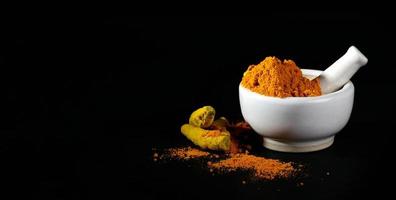 Turmeric powder in mortar with pestle and roots or barks on black background photo