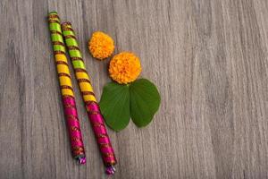 Indian Festival Dussehra and Navratri, showing golden leaf Bauhinia racemosa and marigold flowers with Dandiya sticks on a wooden background photo