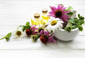 Flores y plantas medicinales en mortero y aceites esenciales sobre una mesa de madera blanca foto