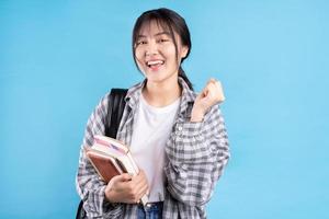 Estudiante asiática con expresión lúdica sobre fondo azul. foto