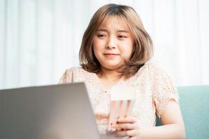 Young Asian girl sitting on sofa eating and watching movies on laptop photo
