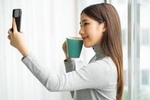Mujer de negocios asiática de pie tomando selfie foto por ventana