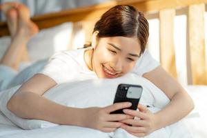 Hermosa mujer asiática usando su teléfono cuando se despierta foto