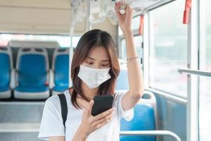 Chica asiática con máscara mientras usa el teléfono inteligente en el autobús foto