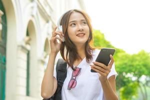 Joven asiática leyendo un texto en su teléfono y usando audífonos para escuchar música en la calle