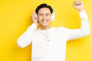 Foto de hombre asiático con camisa blanca escuchando música con los ojos cerrados sobre fondo amarillo