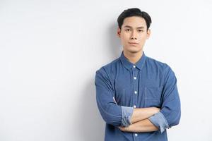Foto de un empresario asiático de pie con los brazos cruzados y sonriendo sobre un fondo blanco.