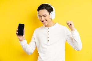 El empresario asiático está escuchando música con auriculares inalámbricos, sosteniendo un teléfono inteligente ming en la mano foto