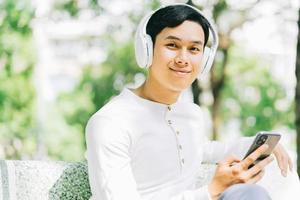 apuesto hombre asiático está usando su teléfono para escuchar música en el parque foto