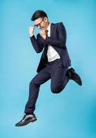 Asian buisnessman wearing suit and jump up on blue background photo