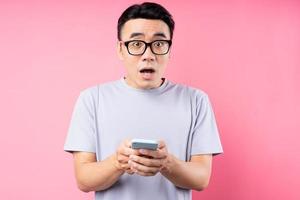 Portrait of Asian man using smartphone on pink background photo