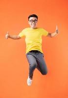 Hombre asiático en camiseta amarilla saltando sobre fondo naranja