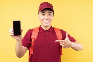 Asian delivery man wearing a red uniform posing on yellow background photo