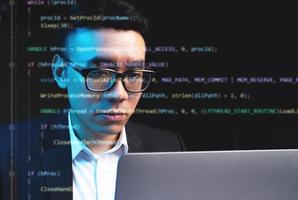 Hombre asiático que se centra en la programación con líneas de código que se ejecutan en la pantalla foto