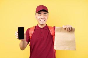Asian delivery man wearing a red uniform posing on yellow background