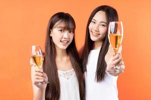 Dos hermosas jovencitas asiáticas levantando copas de vino sobre fondo naranja