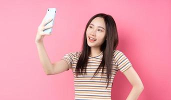 Young Asian woman using smartphone on pink background photo