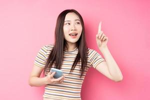 Joven mujer asiática con smartphone sobre fondo rosa