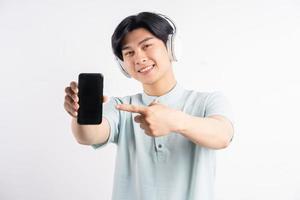 Hombre asiático lleva auriculares y apunta con el dedo al teléfono con pantalla en blanco foto