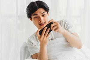 Hombre asiático está usando su teléfono para jugar en la cama foto