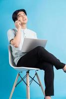 Hombre asiático sentado en una silla mientras usa la computadora portátil mientras realiza una llamada foto